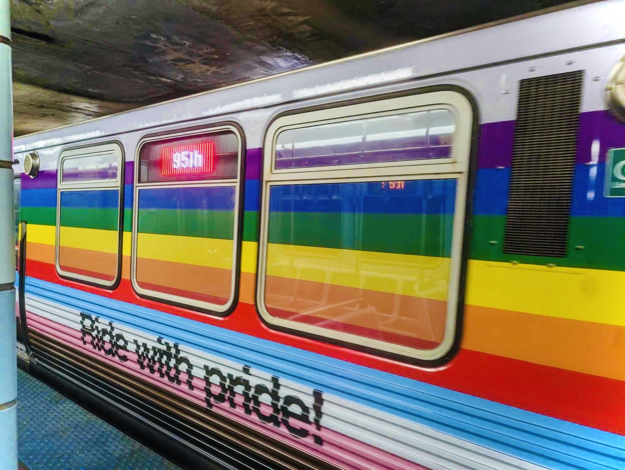A CTA train care decorated with large progressive rainbow colors and the words "Ride with pride!"